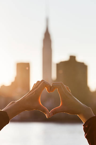 istock Heart Shaped Hands at Sunset, New York Skyline on Background 515836283