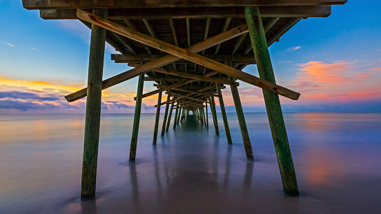 The rising sun paints the sky over the sea with vivid colors as seen from beneath the Bogue Inlet Fishing Pier in Emerald Isle, North Carolina.