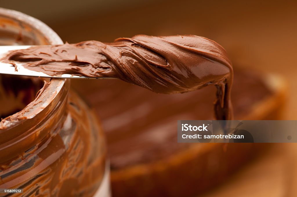 Knife full of sweet chocolate nougat spread on glass jar. Chocolate Stock Photo