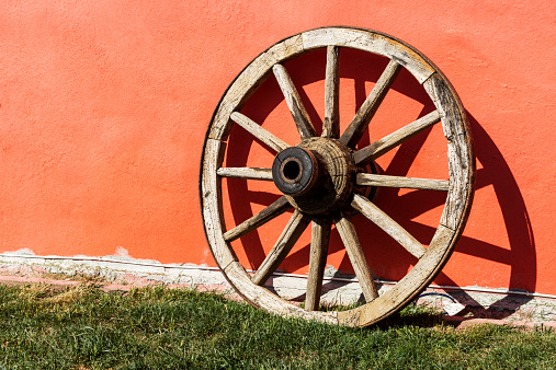 Old fashioned wheel front of wall.