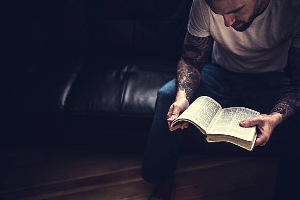 Man Reading Bible An overhead view of a man reading scripture in a dark room, window light illuminating the pages from above and behind him.  Horizontal image with copy space. Bible stock pictures, royalty-free photos & images