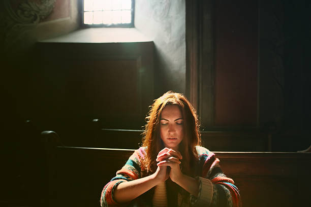 Silhouette of a woman seated in front of a stained glass window of a church
