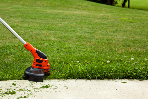 Close-up of a string trimmer cutting the grass along a concrete sidewalk.
