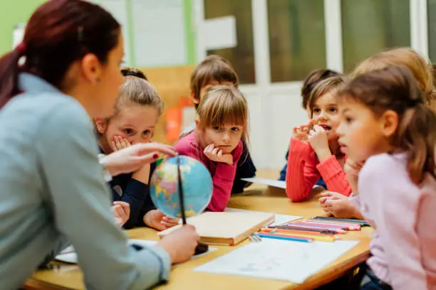 Photo of Preschool teacher and children using globe.