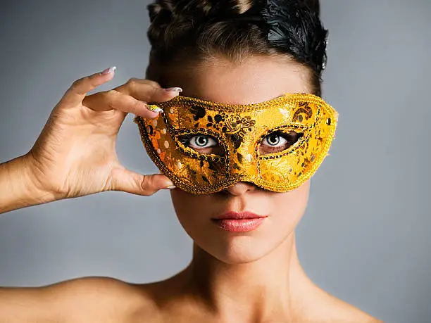 Close-up portrait of attractive fashion model hiding face behind golden mask. Studio shot.