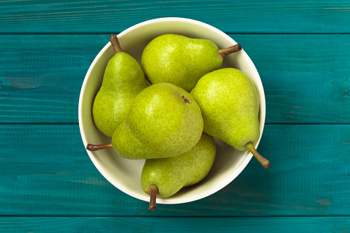 fresh juicy green pears in white bowl on blue wooden background, top view. rustic style.
