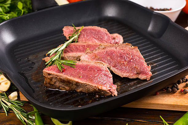 Slices of Rare Beef Sizzling on Cast Iron Fry Pan Close Up of Slices of Rare Roast Beef Frying on Ridged Skillet Cast Iron Pan and Seasoned with Fresh Herbs of Rosemary griddle stock pictures, royalty-free photos & images