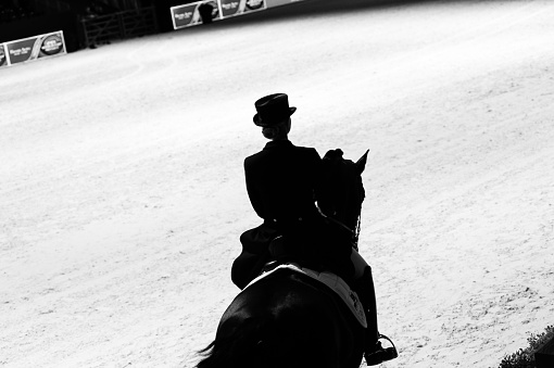 In an equestrian center, a young male jockey is riding a beautiful gray-haired thoroughbred horse, the man is wearing a helmet and safety equipment. They are performing riding exercises. Dressage and riding.