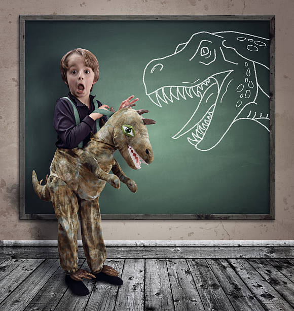 Surprised boy dressed in fancy dress as a dinosaur Surprised boy dressed in fancy dress as a dinosaur with chalk tyrannosaurus rex on blackboard concept for education, history, science and imagination tyrannosaurus rex photos stock pictures, royalty-free photos & images