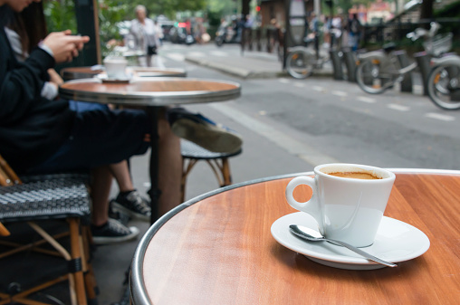 A cup of coffee on the table at the terrace of a cafe in Paris, France. The white pottery is placed on the wooden table of the coffee shop which faces the street. (XXXLarge)