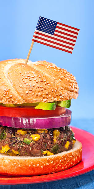 Healthy Beef Hamburger with American flag A healthy, low-fat beef hamburger with chili peppers, black beans, corn, cilantro, green onions, with red onion, tomato and avocado slices on a sesame seed bun. Shallow depth of field. American flag stuck in the top toothpick stock pictures, royalty-free photos & images
