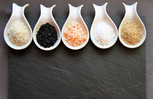 Variety of Different Sea Salts in spoons on on a black slate stone background