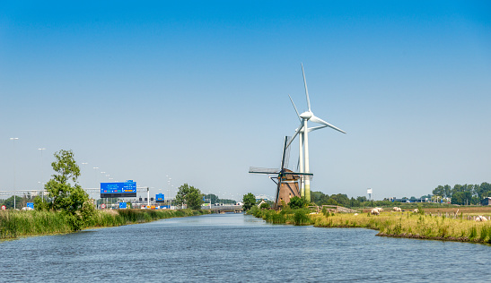 Durable energy wind mills and wind turbines next to each other, generating electricity. On the left side the A4 highway. Seen from the water. Shot from the Meerburger Watering near Leiden