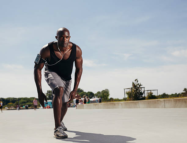 Fit young man on his mark to start running. Determined athlete outdoors. Muscular african male model ready for his run on a hot summer day.