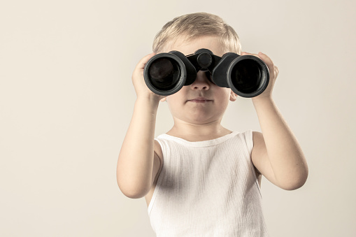 A young boy looking through binoculars with copy space tot he left (stock image).