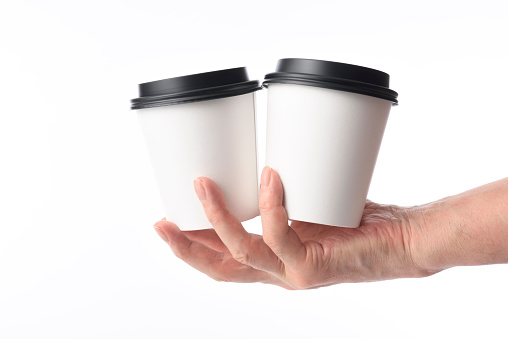 Holding two blank disposable paper coffee cup against white background.
