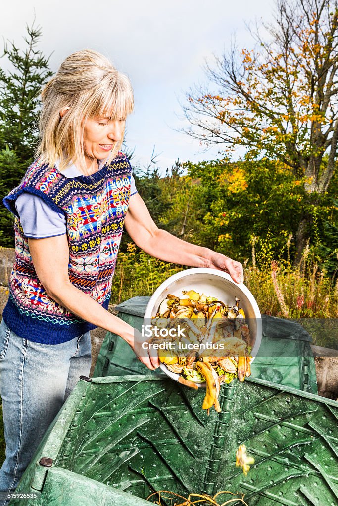 Woman recycling vegetable waste in compost bin Woman throwing fruit and vegetable waste into a garden compost bin. AdobeRGB colorspace. Compost Stock Photo