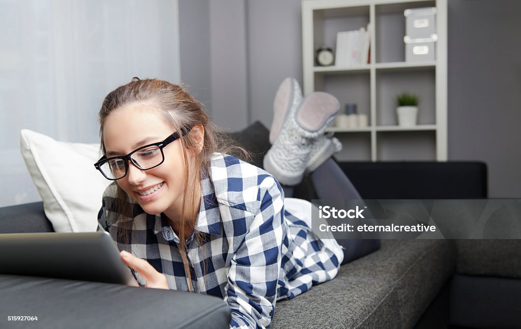 Using Digital Tablet on Sofa Young woman lying on the couch at home and using a digital tablet 20-29 Years Stock Photo