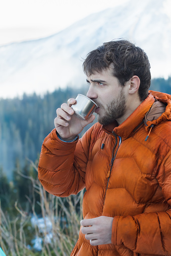 Portrait of resting mountaineer with hot drink metal vacuum flask at snowy winter mountains background