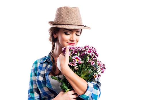 Beautiful young woman in blue checked shirt  and hat holding a bouquet of chrysanthemum flowers, smelling them. Studio shot on white background.