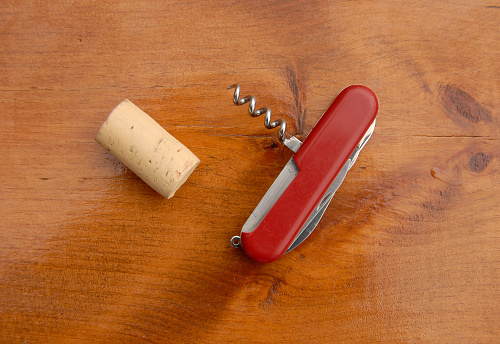 Swiss knife, corkscrew and cork on wood background