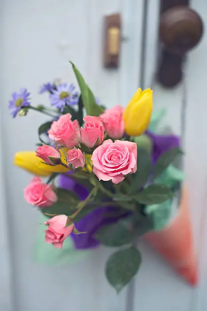 A paper cone full of bright flowers hangs on a front doorknob celebrating May Day.  But can be any holiday really, mothers day, valentines day, a birthday. Beautiful flowers in a hand made paper cone. 