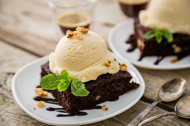 Chocolate brownie with vanilla ice cream, nuts and mint Chocolate brownie with vanilla ice cream, nuts and mint, served om white plate, rustic wood background theobroma stock pictures, royalty-free photos & images