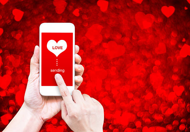 mano che tiene il telefono intelligente con l'invio di amore e cuore parola - business blurred motion text messaging defocused foto e immagini stock