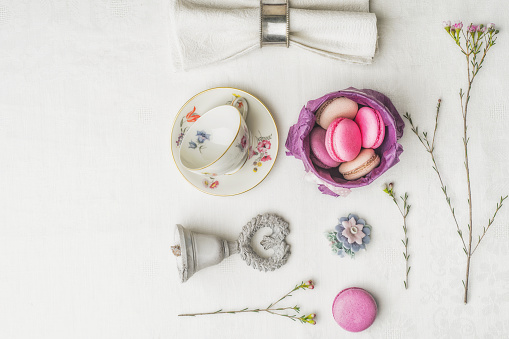 Macaroons with flowers , bell , cup and napkin on the white cloth top view