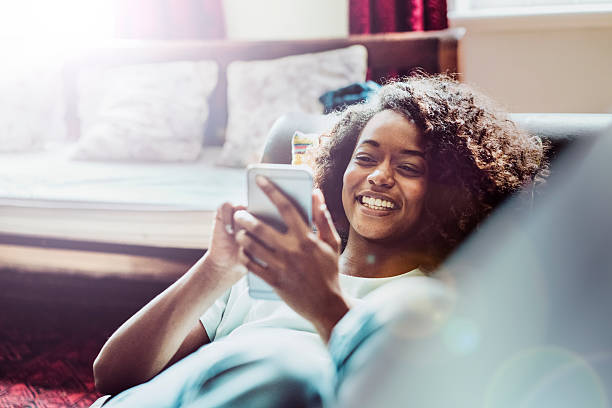 femme heureuse à l'aide de téléphone portable sur un canapé - cheveux mi longs photos et images de collection