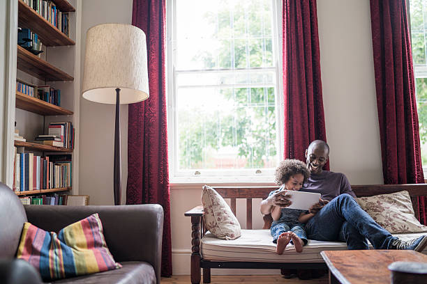 feliz hombre con hija usando tableta digital en sofá - lámpara de piso fotografías e imágenes de stock