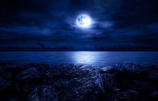 Full moon over the ocean with clouds and rocks
