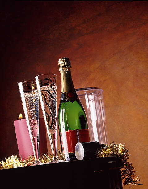glasses filled with champagne and bottle on table, with pink candle and decoration in the background the yellow-brown wall of a wine cellar.
