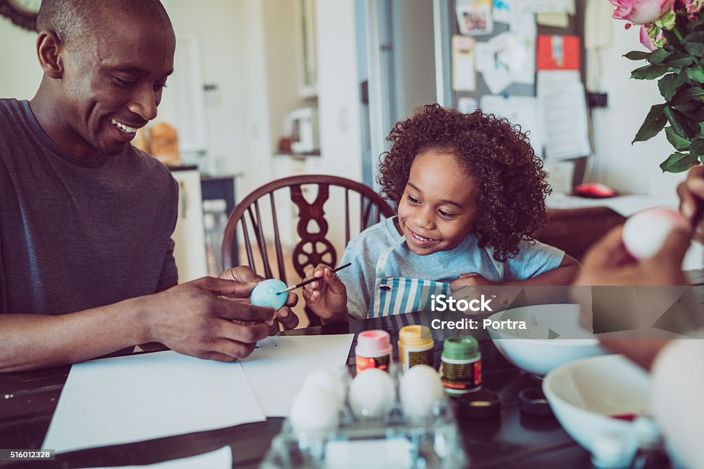 Father and boy colouring Easter egg together A photo of father and boy colouring Easter egg together. Happy man holding egg for son. They are sitting at table. Easter Stock Photo