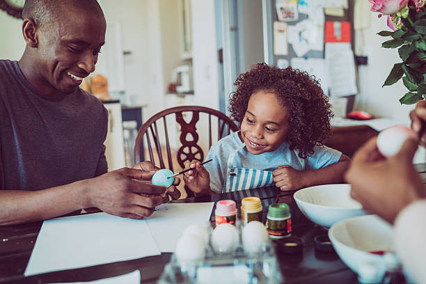 Father and boy colouring Easter egg together A photo of father and boy colouring Easter egg together. Happy man holding egg for son. They are sitting at table. easter egg coloring stock pictures, royalty-free photos & images
