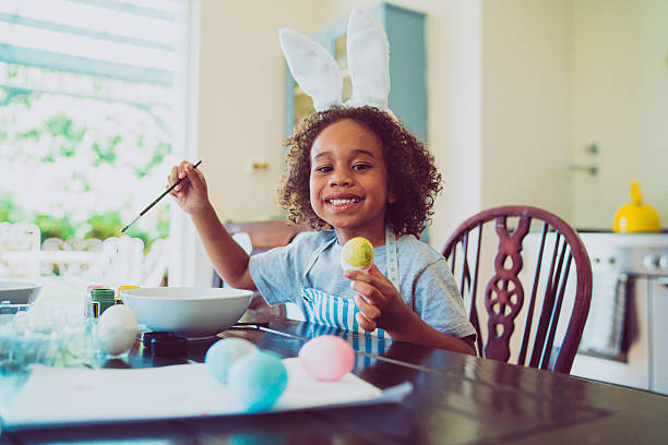 Happy boy coloring Easter egg at home A photo of happy boy colouring Easter egg. He is holding paintbrush and egg. Portrait of little male is sitting at table in home. children only stock pictures, royalty-free photos & images