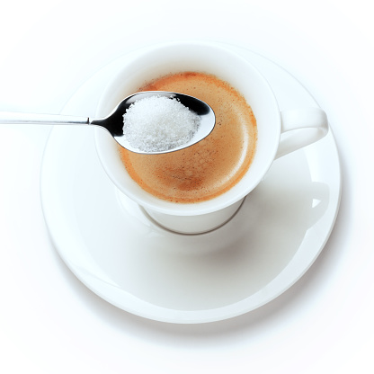 A glass of fresh coffe with sugar in a teaspoon. Isolated on white..
