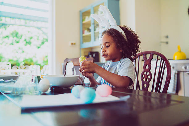 Boy looking at coloured Easter egg A photo of boy looking at coloured Easter egg. He is wearing bunny ears at table. Little male is holding egg at home. children only stock pictures, royalty-free photos & images