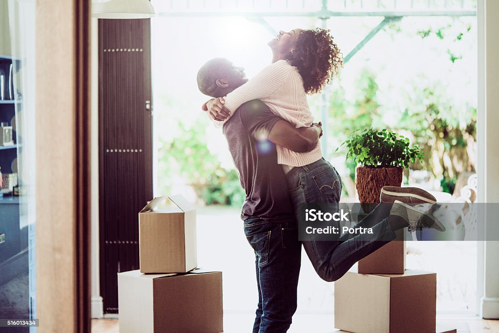 Happy man lifting woman in new house A photo of happy man lifting woman in new house. Side view of loving and excited couple are in casuals. They are with cardboard boxes at entrance. Moving House Stock Photo