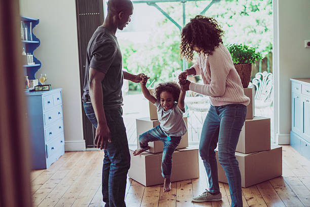 Playful parents holding son's hands in new house A photo of playful parents holding sons's hands in new house. Happy and playful family are with cardboard boxes. They are in casuals. young family stock pictures, royalty-free photos & images