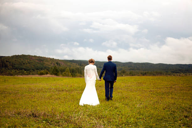 jeunes mariés marchant dans le champ - wedding suit photos et images de collection