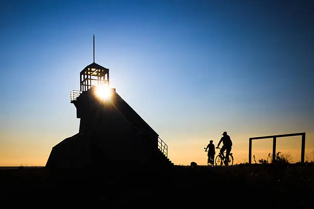 Two bicyclists arriving to a lighthouse during the sunset