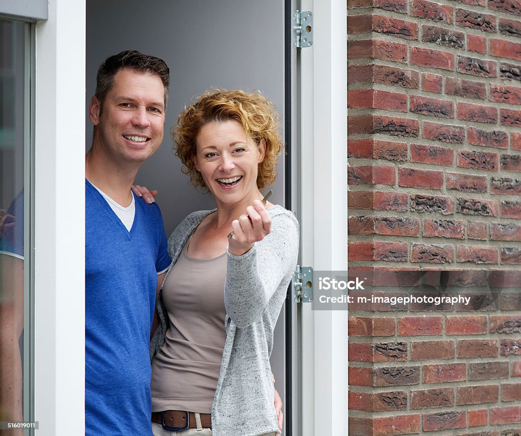 Couple standing by door of new home holding keys Portrait of a cheerful couple standing by door of new home holding keys Front Door Stock Photo