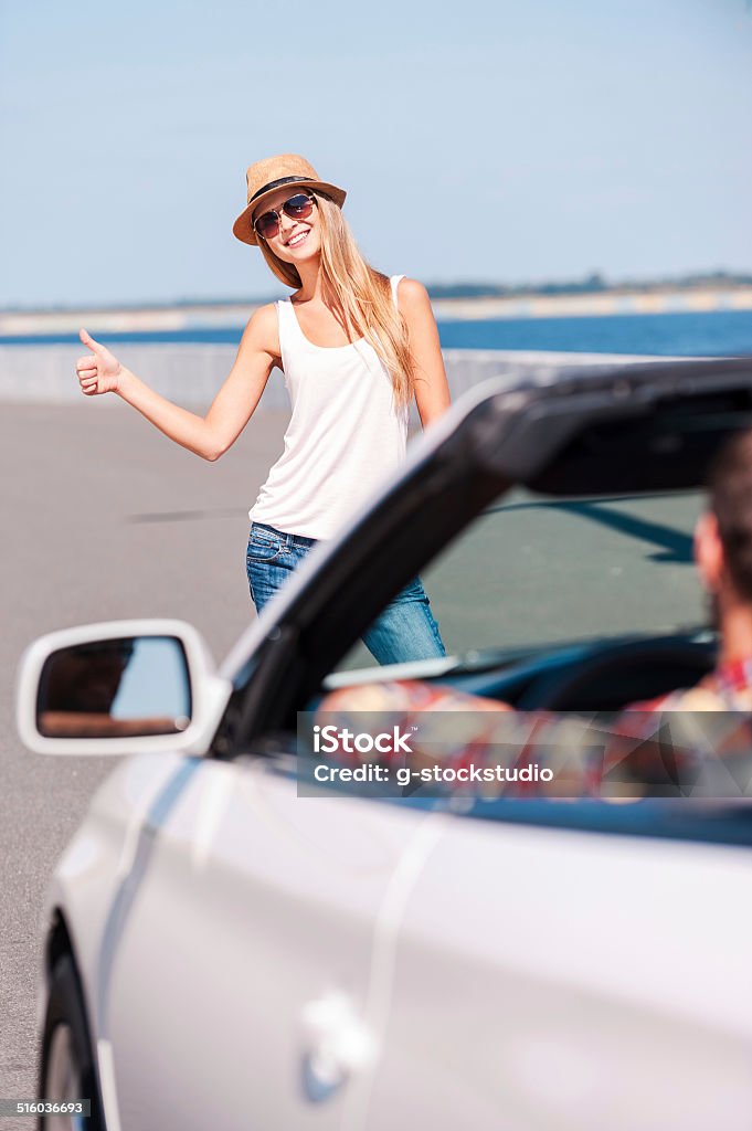 Woman hitching a ride. Beautiful young funky woman hitch-hiking on the side of the road with car on foreground Adult Stock Photo