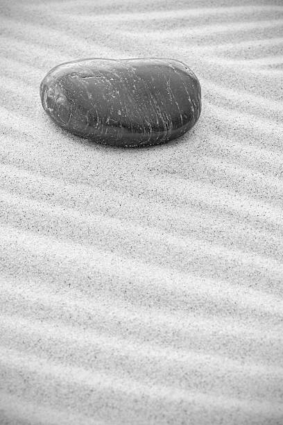 istock Black and white picture of a stone on sand. 516038318