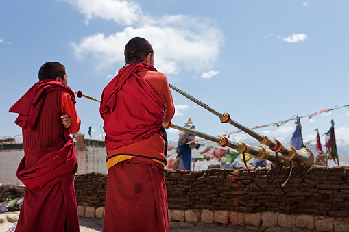 Young Tibetan monks playing buddhist horns on the roof of monastery in Lo Manthang. Mustang region is the former Kingdom of Lo and now part of Nepal,  in the north-central part of that country, bordering the People's Republic of China on the Tibetan plateau between the Nepalese provinces of Dolpo and Manang. The Kingdom of Lo, the traditional Mustang region, and “Upper Mustang” are one and the same, comprising the northern two-thirds of the present-day Nepalese Mustang District, and are well marked by official “Mustang” border signs just north of Kagbeni where a police post checks permits for non-Nepalese seeking to enter the region, and at Gyu La (pass) east of Kagbeni.http://bem.2be.pl/IS/mustang_380.jpg