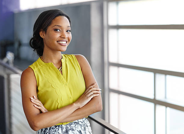 Portrait of a confident black businesswoman at work in her Friendly african american woman standing with arms crossed in a modern bright office black woman hair bun stock pictures, royalty-free photos & images