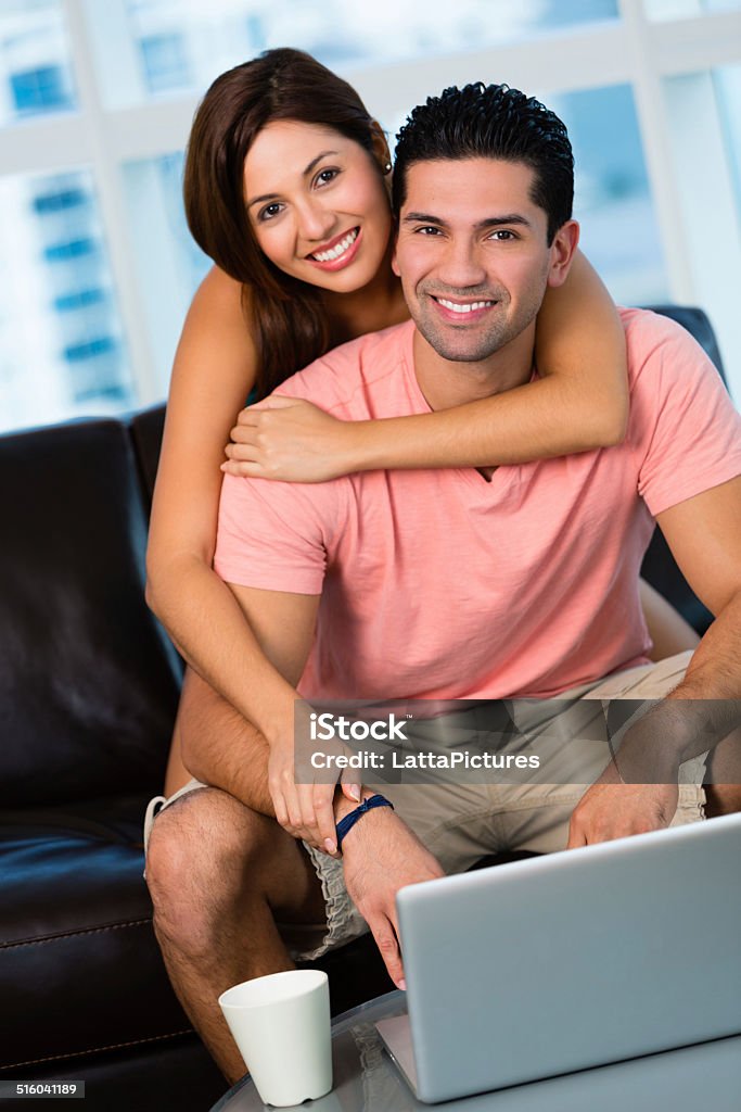 Smiling couple looking at camera Young Hispanic couple sitting on couch with laptop, female has arm around male 20-29 Years Stock Photo
