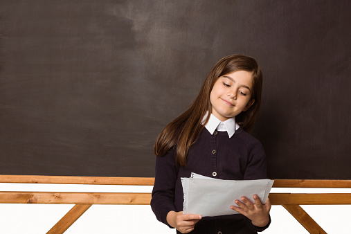 Cute pupil holding white pages in classroom