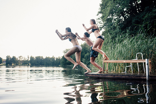 three young adults jumping into a lake